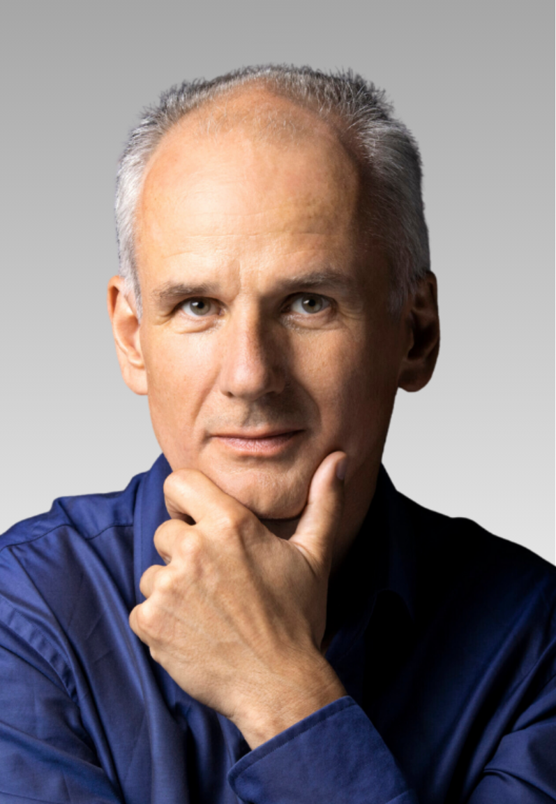 Portrait photograph of Prof Nikolaus Rajewsky. Elegantly dressed man with grey hair, supporting his chin with his hand, smiling slightly.