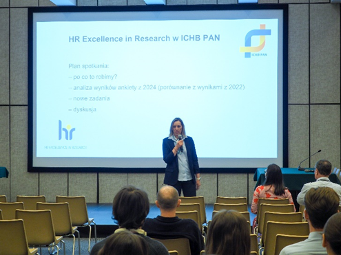 Dr hab. Luiza Handschuh, prof. ICHB PAN, Dyrektor Instytutu, przedstawia plan spotkania zgromadzonym pracownikom. W tle wyświetla się slajd z agendą wydarzenia.