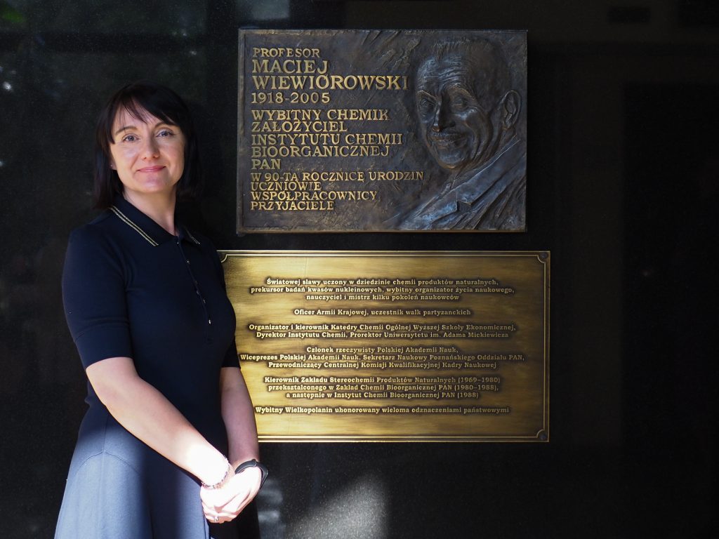 Elegancko ubrana i uśmiechnięta Monika Piwecka przy tablicy upamiętniającej prof. Macieja Wiewiórowskiego