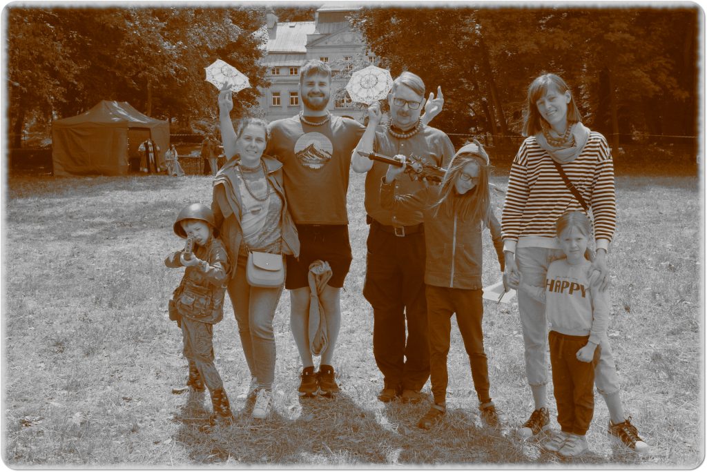 Sepia photo: a smiling family of seven; behind them, a meadow and a palace