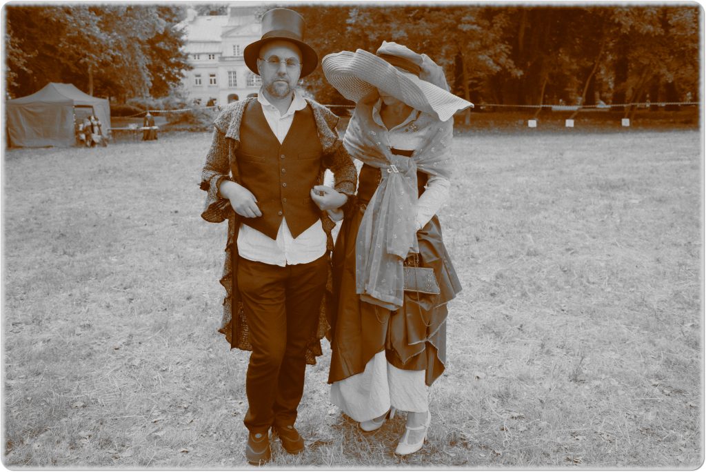 Sepia photo: a woman and a man dressed in historical costumes; behind them, a meadow and a palace