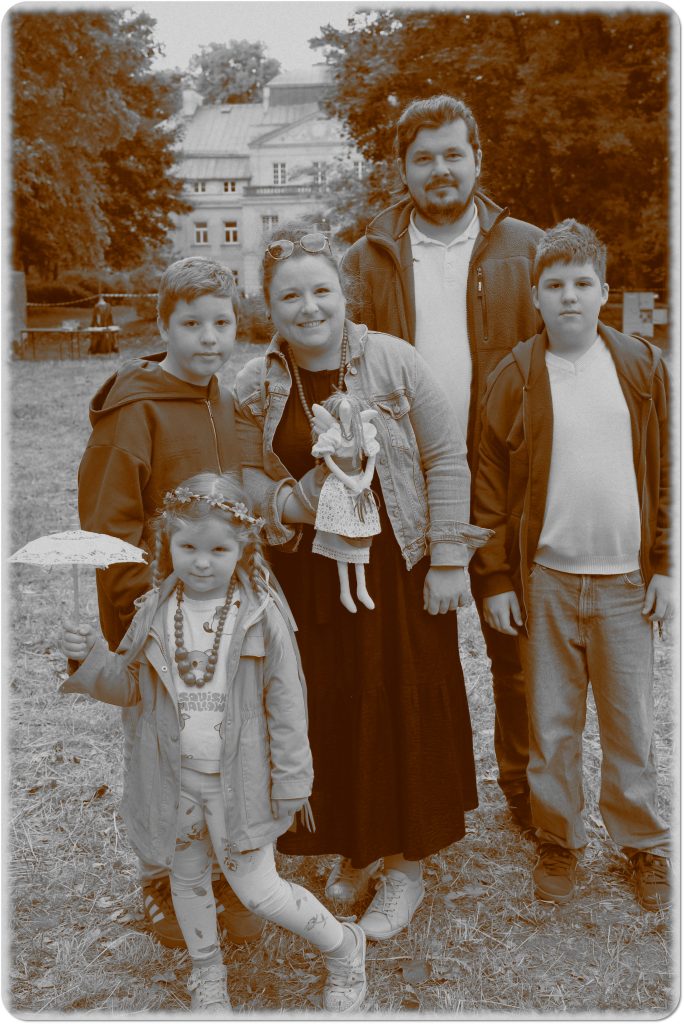 Sepia photo: a smiling family; a girl holding an umbrella and a boy with a doll; behind them, a meadow and a palace