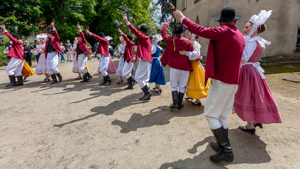 Eight pairs of dancers in folk costumes dancing in front of the palac