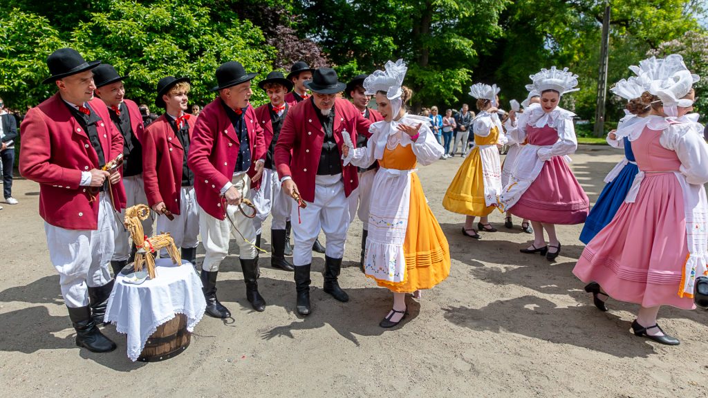 A folk dance group performing a scene in front of the palace; in the foreground, a barrel with a straw horse