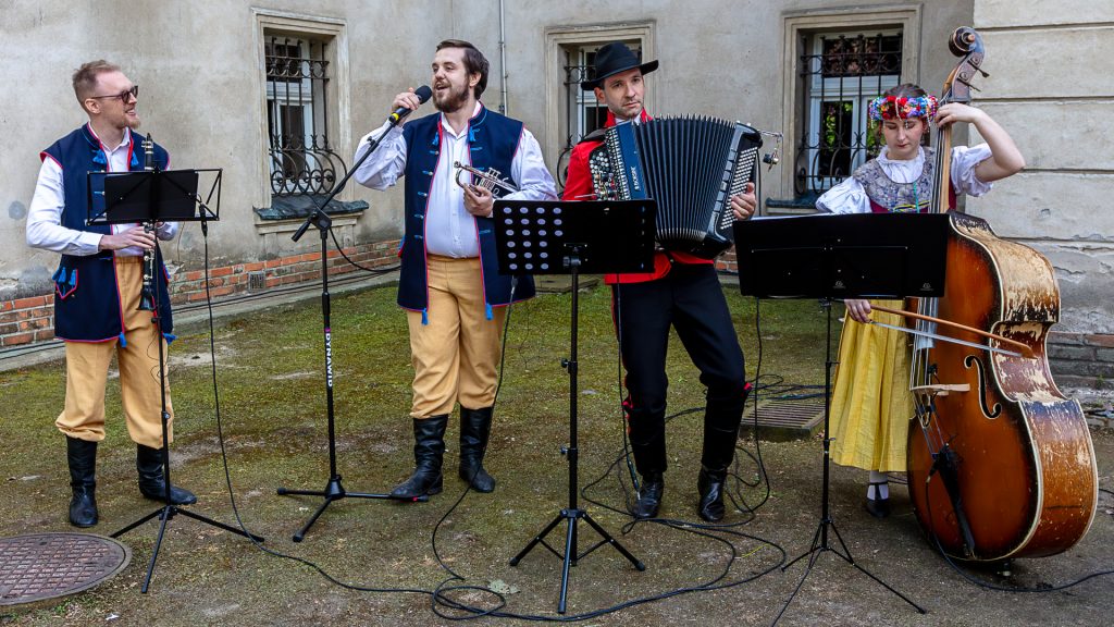 Four folk band members: one singing into a microphone, others playing instruments