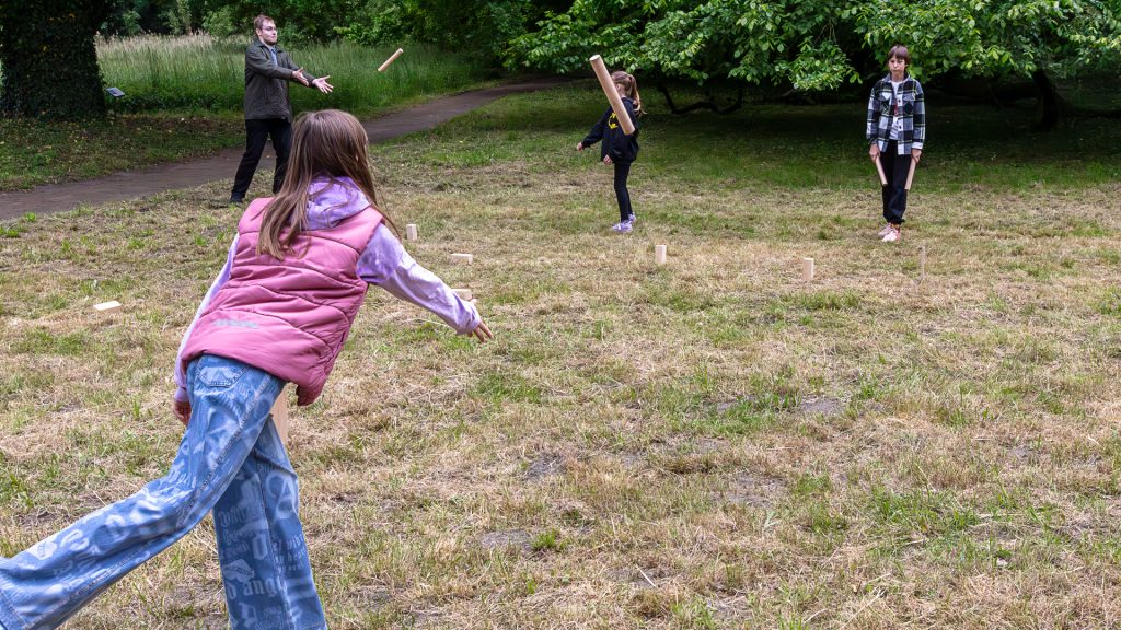On the meadow, people are playing lawn games like croquet and boules