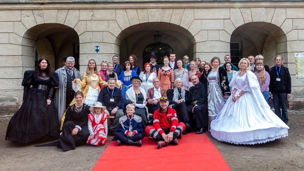A large group of people, some dressed in historical costumes, posing in front of the palace