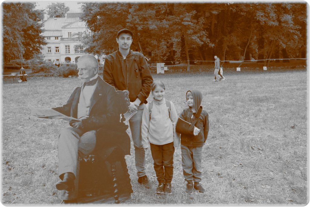 Sepia photo: a man and two children standing by a large photo of General Chłapowski; behind them, a meadow and a palace