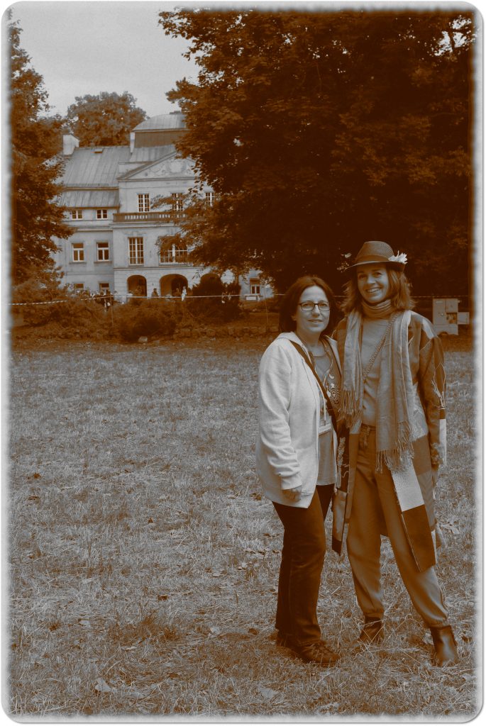 Sepia photo: two smiling women; behind them, a meadow and a palace