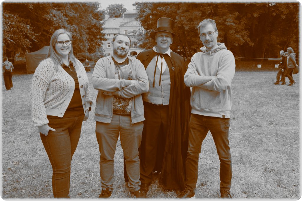 Sepia photo: a woman and three men, one in a top hat and cape; behind them, a meadow and a palace