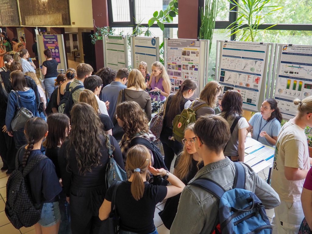 Crowd of young people in the lobby during the Open Doors at IBCH PAS, with posters from scientific publications in the background.