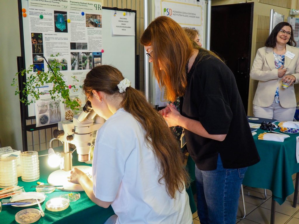 A young girl looking at plant cells in a microscope under the supervision of a scientis