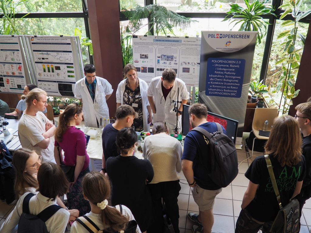A group of young people listening and watching the Medicinal Chemistry Laboratory stand with interest