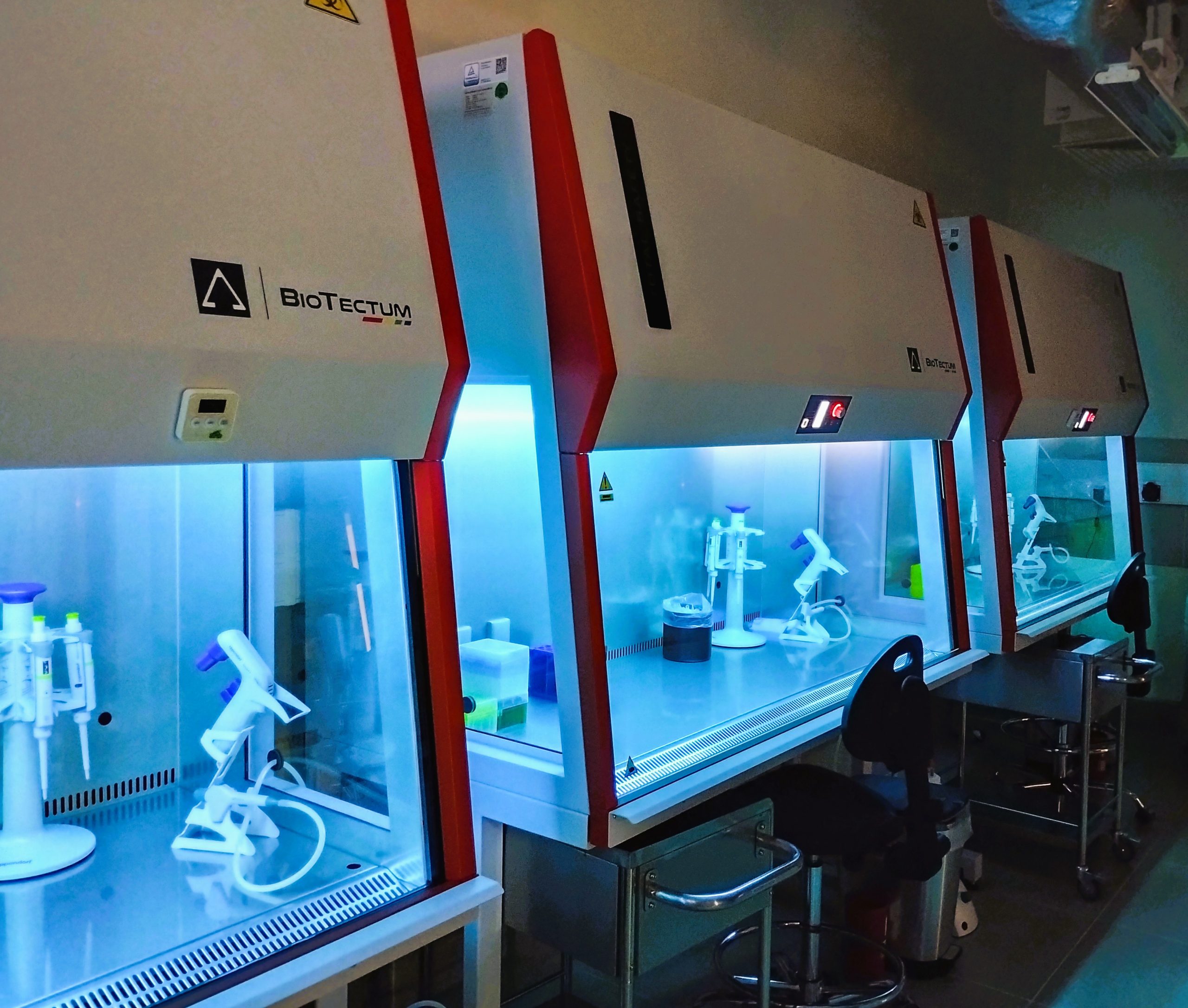 Three laminar flow cabinets standing side by side with UV lamps turned on.