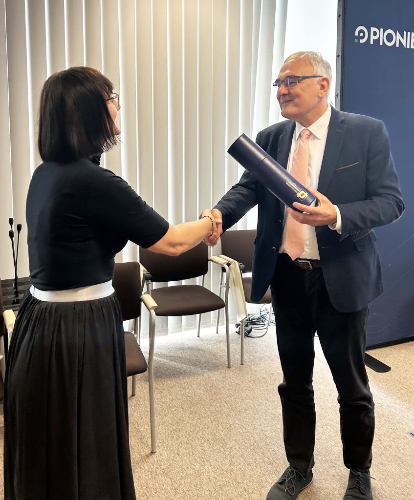 Associate Professor Monika Piwecka receives her habilitation diploma, wrapped in a decorative tube, from Professor Marek Figlerowicz.