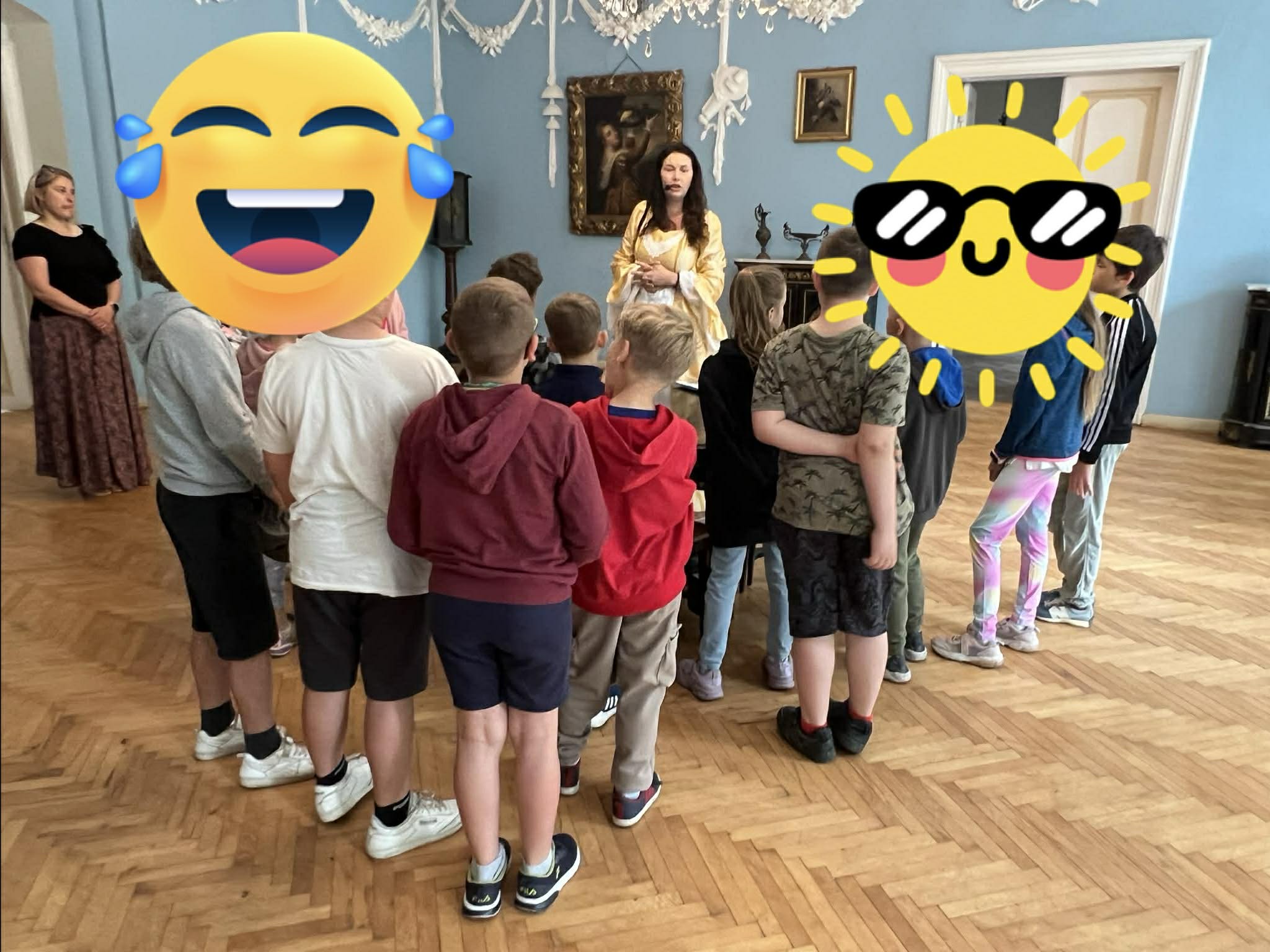 Grupa dzieci w wieku szkolnym w salonie Pałacu w Turwi i jedna kobieta w stroju z epoki