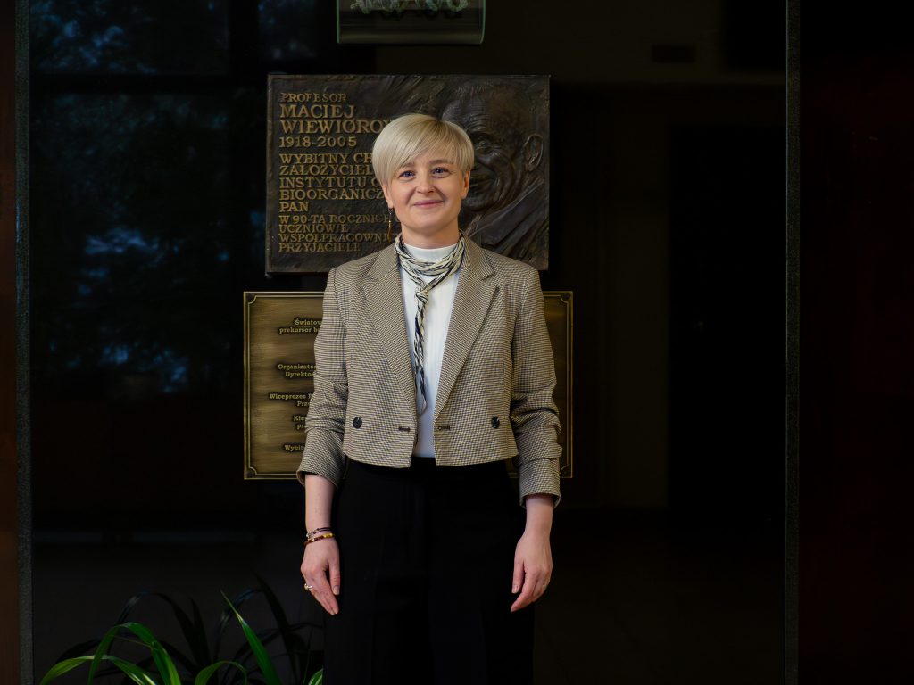 A portrait photograph of Joanna Banasiak next to the commemorative plaque of the Institute’s founder