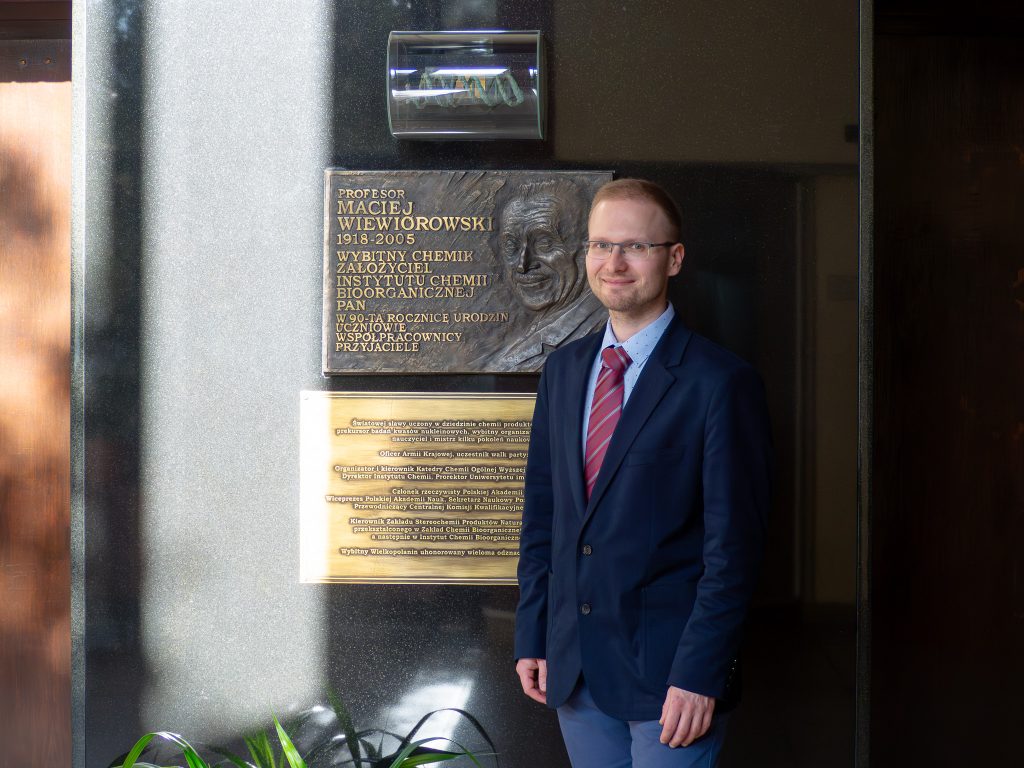 Zdjęcie portretowe Witold Andrałojć przy tablicy pamiątkowej założyciela Instytutu