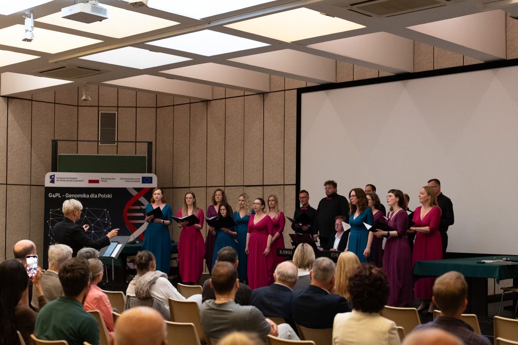 The choir, conducted by a female conductor, is singing a song. In the background, a large screen and the flags of Poland and the European Union are visible.