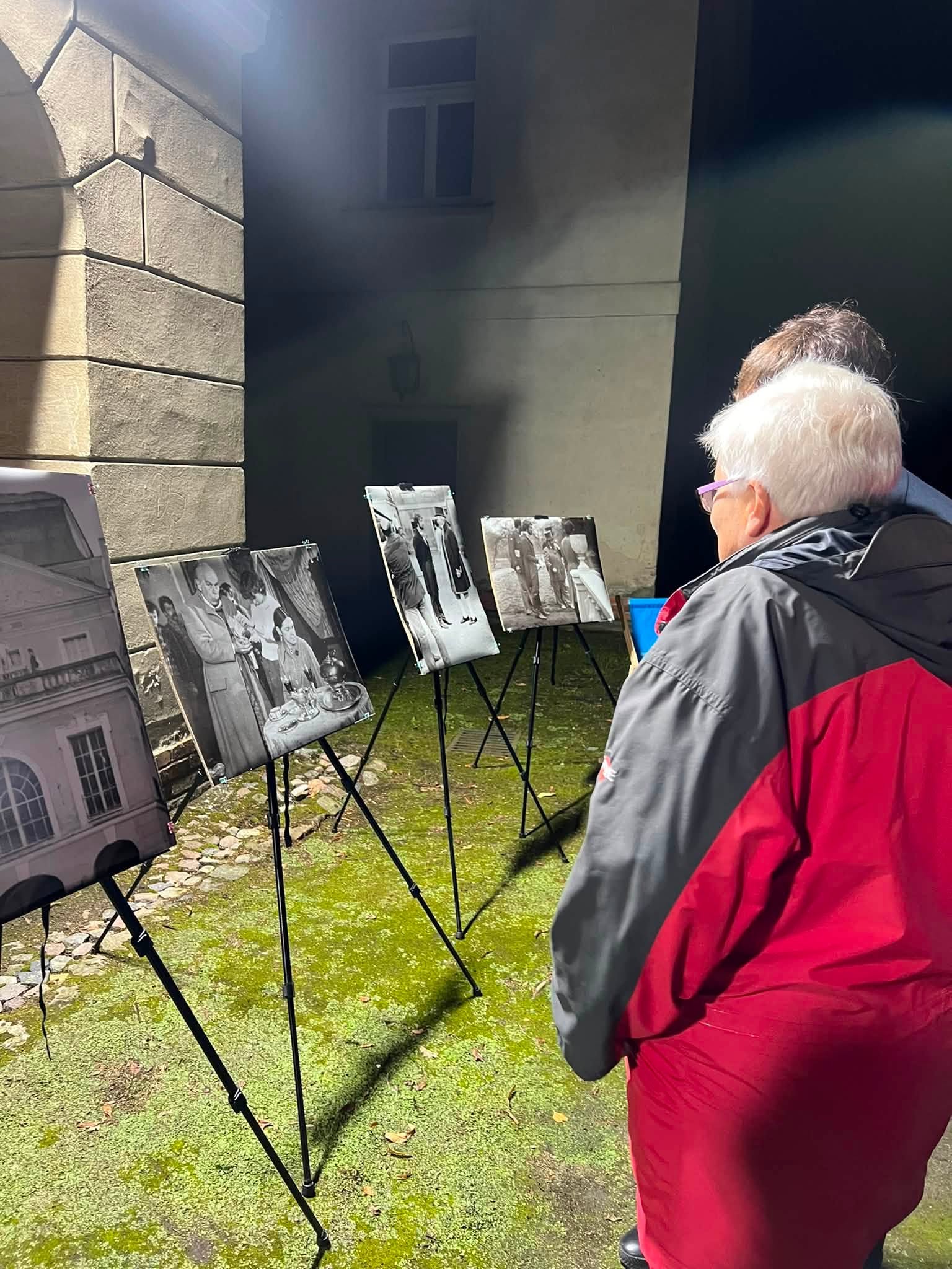 Wystawa fotograficzna. Czarnobiałe fotografie na sztalugach stojące na dziedzińcu przed pałacem i osoby je oglądające