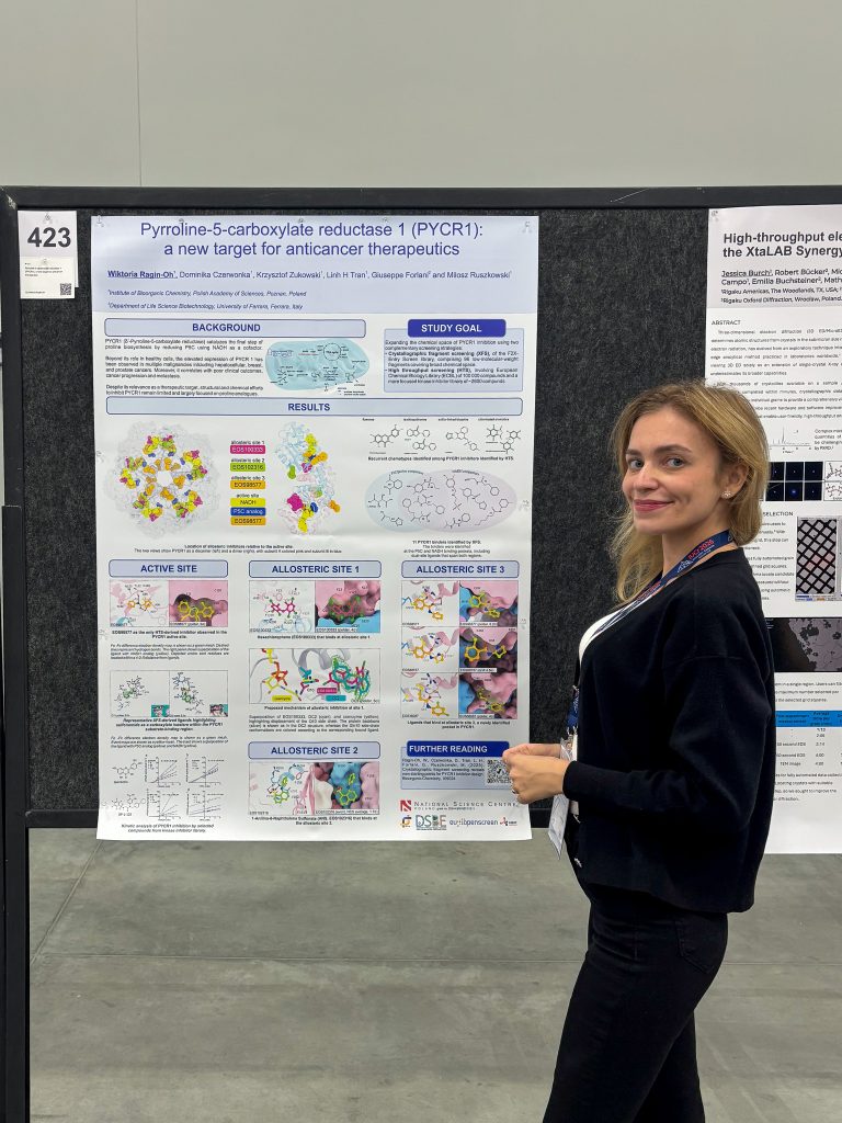 A researcher (a young woman with blonde hair) is standing next to the poster on display, smiling